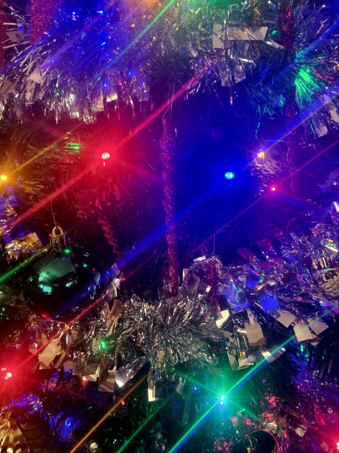 Colorful Christmas lights and shimmering tinsel on a tree.